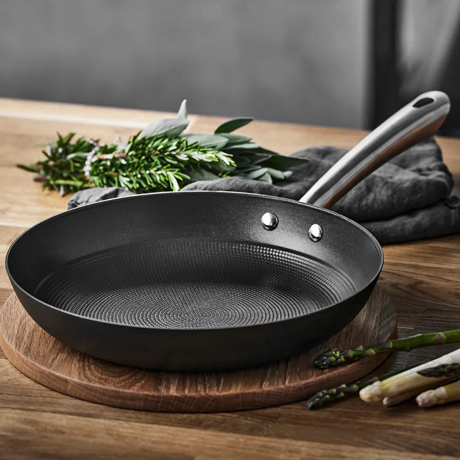 Støpejernspanne med bikubestruktur, presentert på en treplate med grønnsaker i bakgrunnen, ideell for kvalitet matlaging.