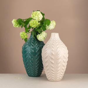 To porselensvaser med bladformet design, en kremfarget og en grønn, fylt med grønne blomster for moderne dekor.