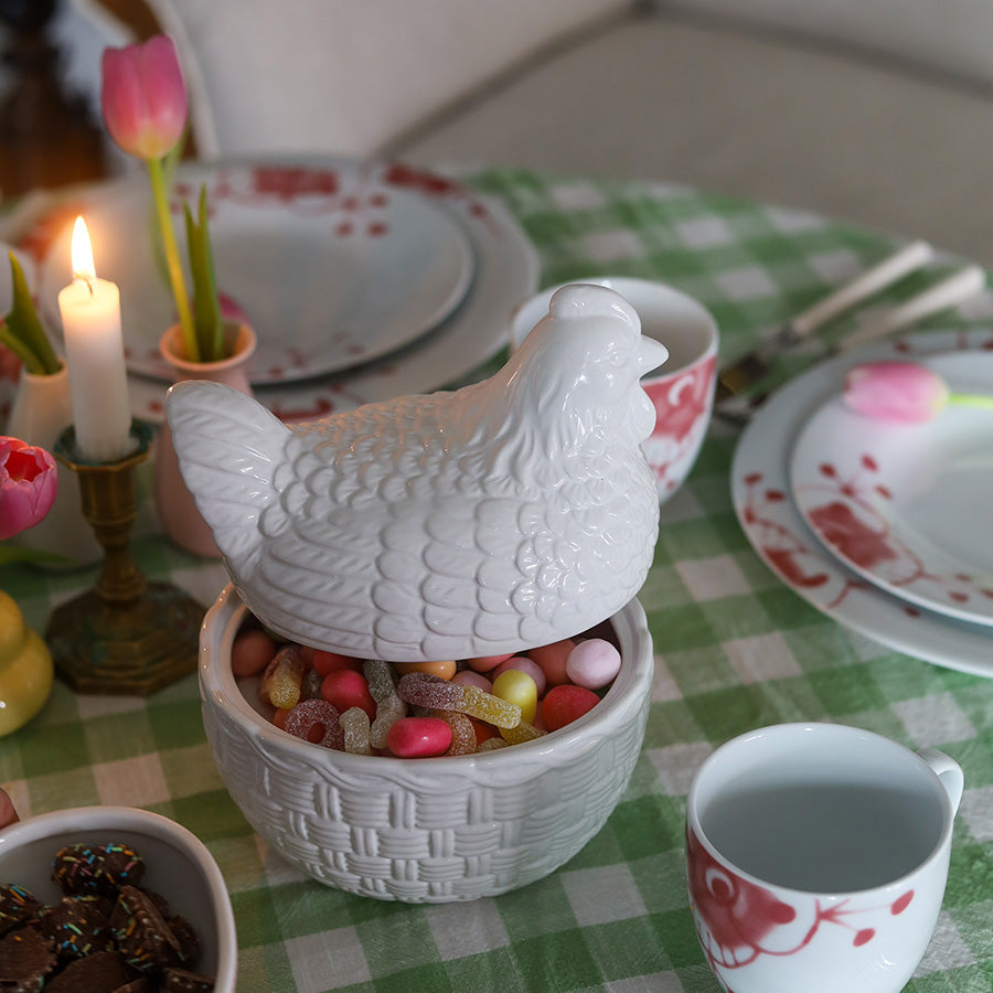 Stilig påskesammensetning med hvit porselen høne og forskjellige tallerkener, gir en klassisk og elegant atmosfære til påskearrangementet.