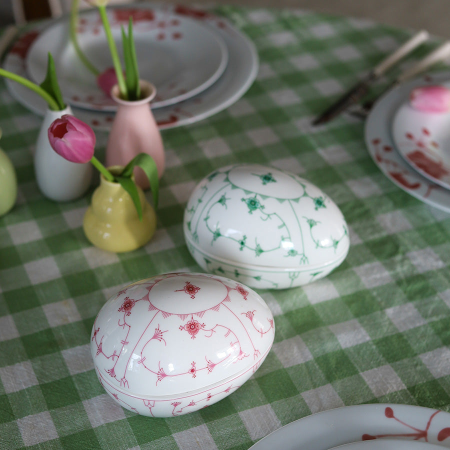 To dekorative påskeegg, ett grønt og ett rosa, fra Porsgrunds Porselænsfabrik, plassert på et rutete bord dekket til påskefest.