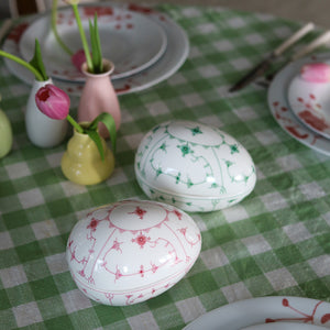 To dekorative påskeegg, ett grønt og ett rosa, fra Porsgrunds Porselænsfabrik, plassert på et rutete bord dekket til påskefest.