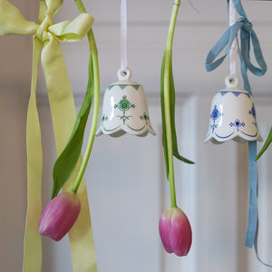 To Porsgrunds Porselænsfabrik bjeller i variert design, hengende med bånd og omkranset av tulipaner, ideelle for vårlig dekorasjon.