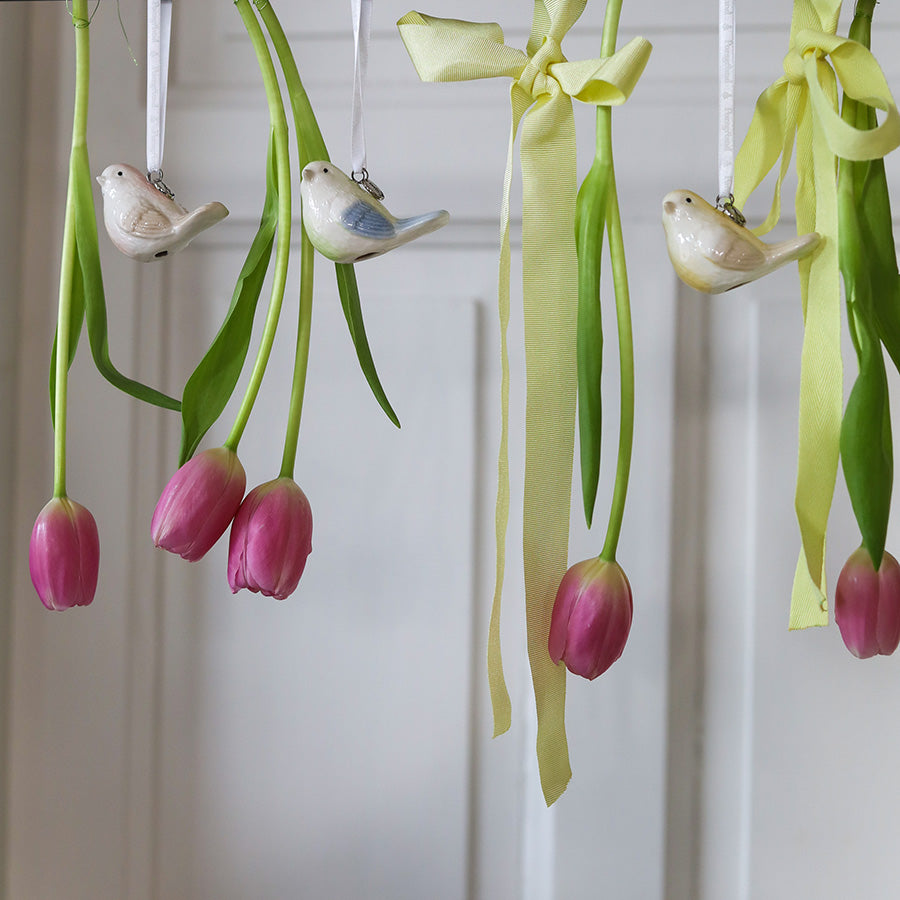 Småfugler i porselen henger mellom freske tulipaner, ideelt for en vårstemning med naturinspirert pynt.