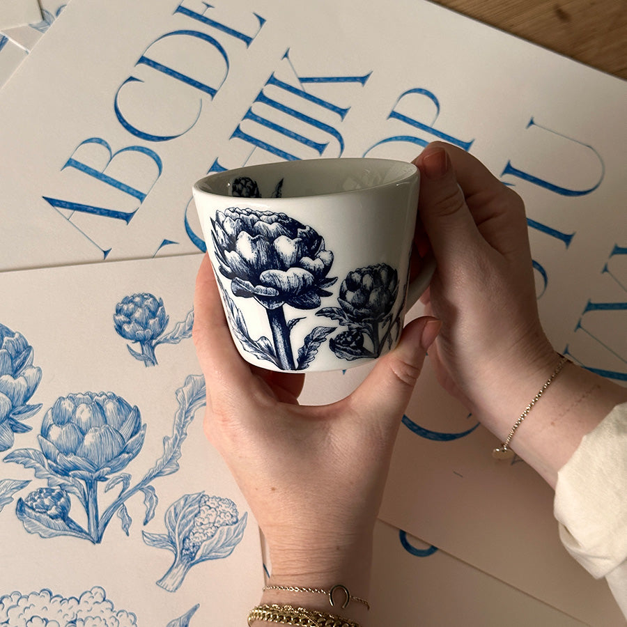 Person som holder bokstavkrus med blomsterdekor, viser det personlige og tidløse designet fra Porsgrunds Porselænsfabrik.
