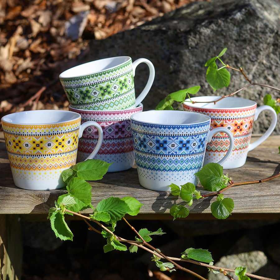 Fire fargerike krus fra Porsgrunds Porselænsfabrik med unike bunadsinspirasjoner, ideelle for å nyte varme drikker.