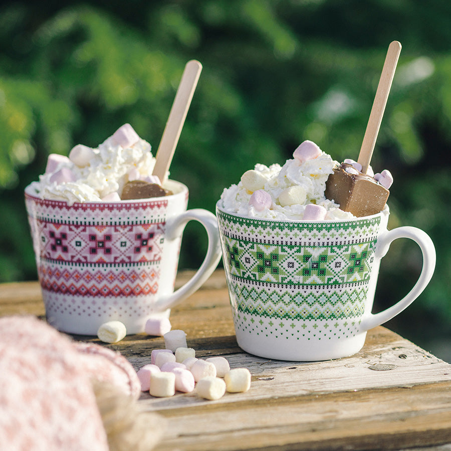 To Ingrid krus, en grønn og en rød, inneholdende kakao med marshmallows, perfekt for kosepauser utendørs.