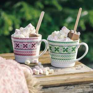 To krus med bunad-inspirert design fylt med skumkrem og marshmallows, ideelt for koselige vinterstunder.