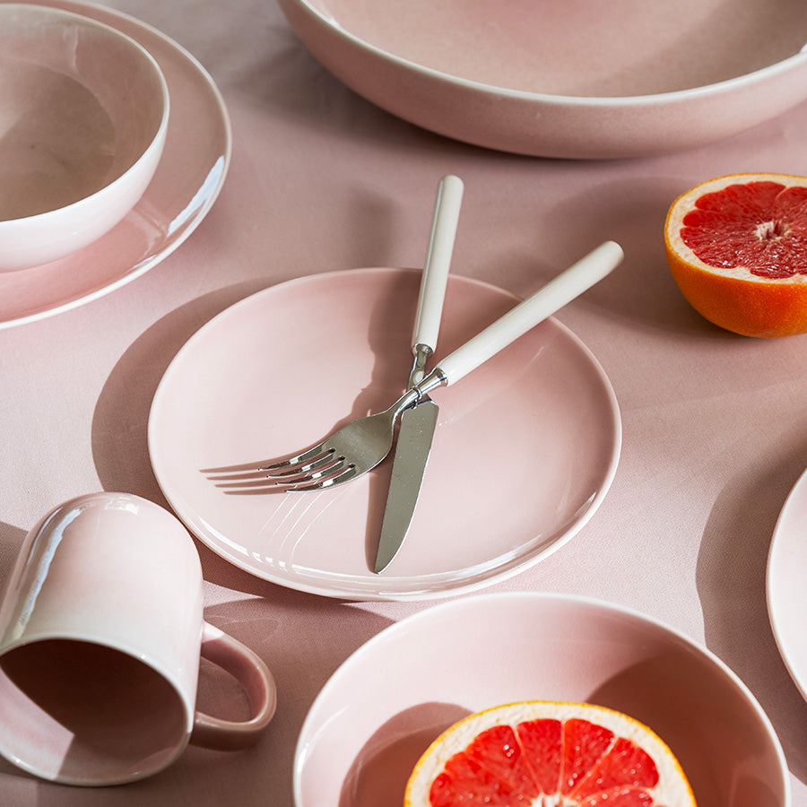 Krus fra Porsgrunds Porselænsfabrik i delikat rose, omgitt av elegant servise og friske citrusfrukter på en rosa duk.