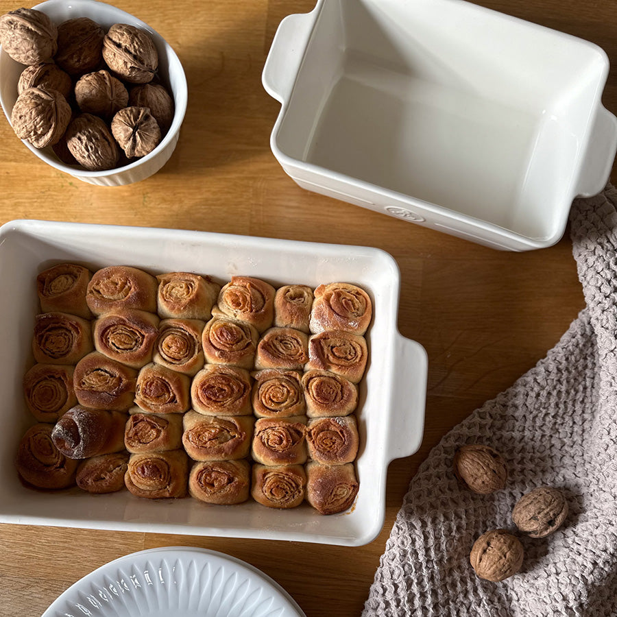 Ildfast form i hvitt porselen med nystekte kanelsnurrer, samt en tom ildfast form