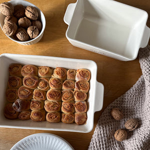 Ildfast form i hvitt porselen med nystekte kanelsnurrer, samt en tom ildfast form