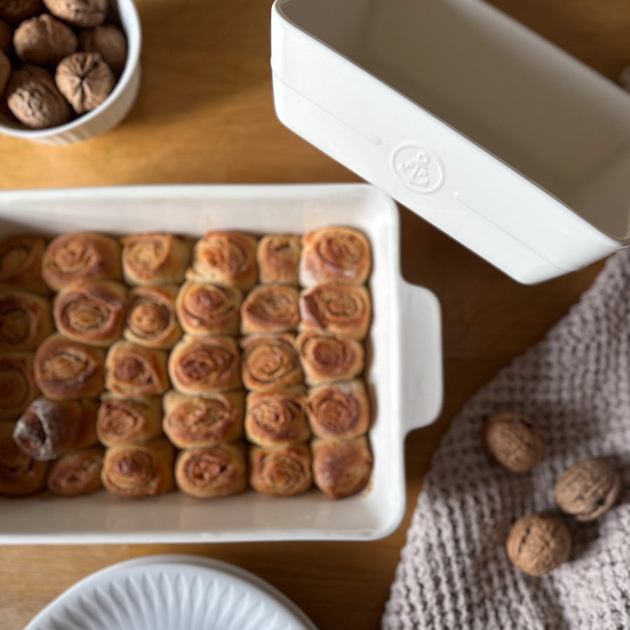 Hvite ildfaste former med porselensdetaljer og nystekte kanelsnurrer på trebord