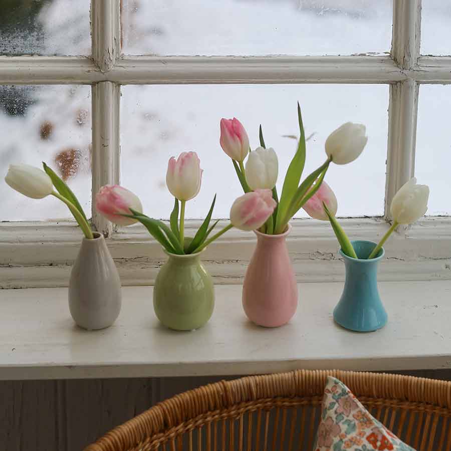 Fire fargerike minivaser med tulipaner på en vinduskarm, med snø utenfor.