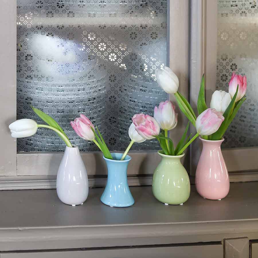 Minivaser med tulipaner ved vinduet, med dekorativt mønster på glasset i bakgrunnen.