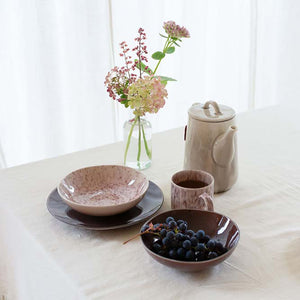 Tallerkener fra Porsgrunds Porselænsfabrik i burgunder og brunt kombinert med en blomsterdekorert vase og serveringsutstyr, for en stilfull borddekking.