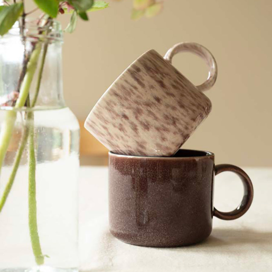 To Porsgrunds Porselænsfabrik Natur Krus, ett i fargen Lyng og ett i en dyp brun nyanse, stablet oppå hverandre på et bord.