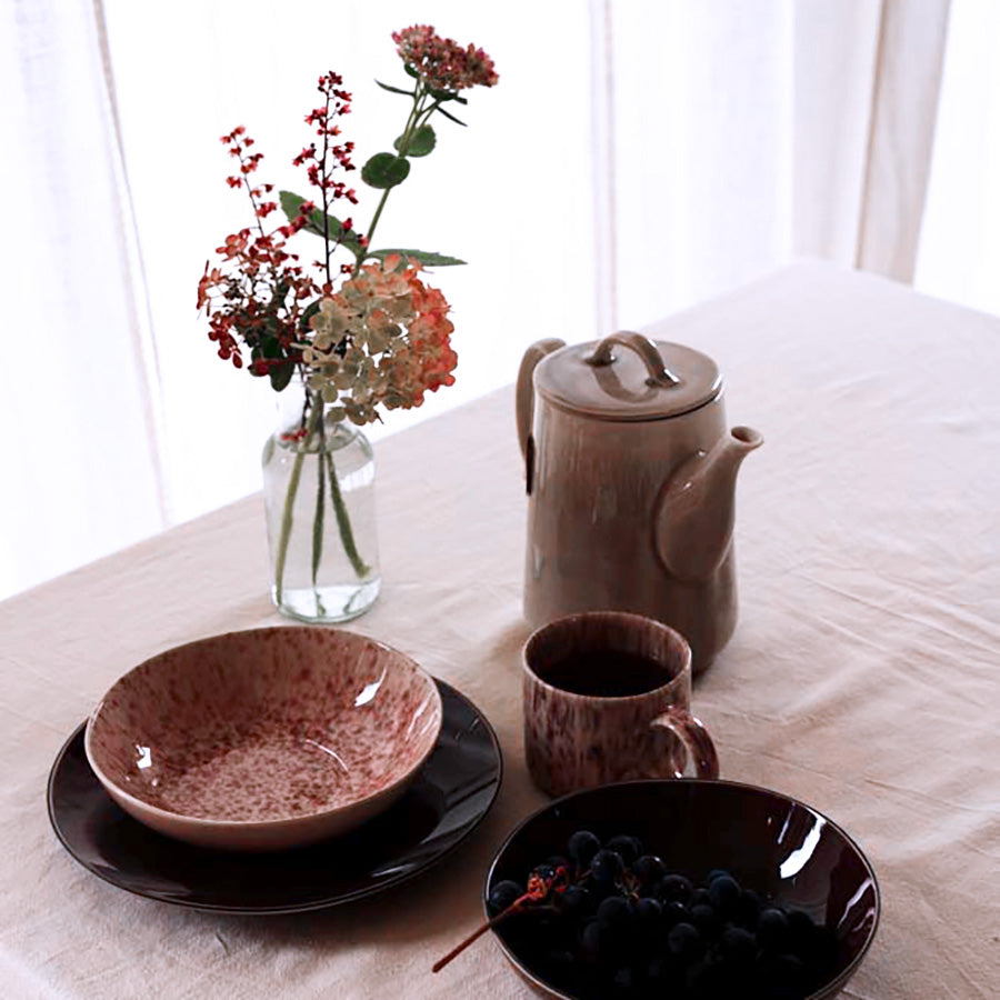 Stilren borddekkingsscene med dyp tallerken, krus og tekanne, dekorert med blomster, ideelt for et koselig måltid.