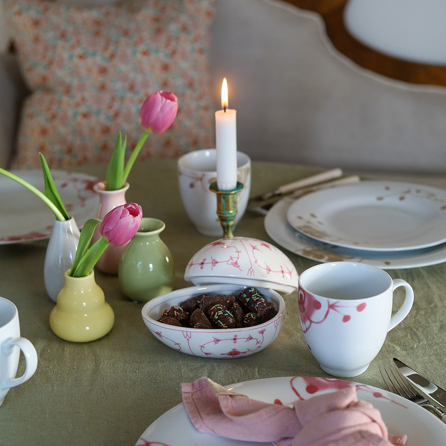 Dekoratørbildet viser minivaser i porselen plassert på et bord med tulipaner og levende lys, skaper en koselig atmosfære til borddekkingen.