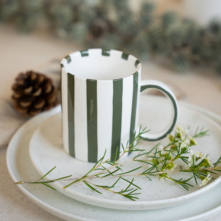 Julekopp fra Porsgrunds Porselænsfabrik med grønne striper, plassert på en tallerken med granbar og kongler, ideell for julekaffe.