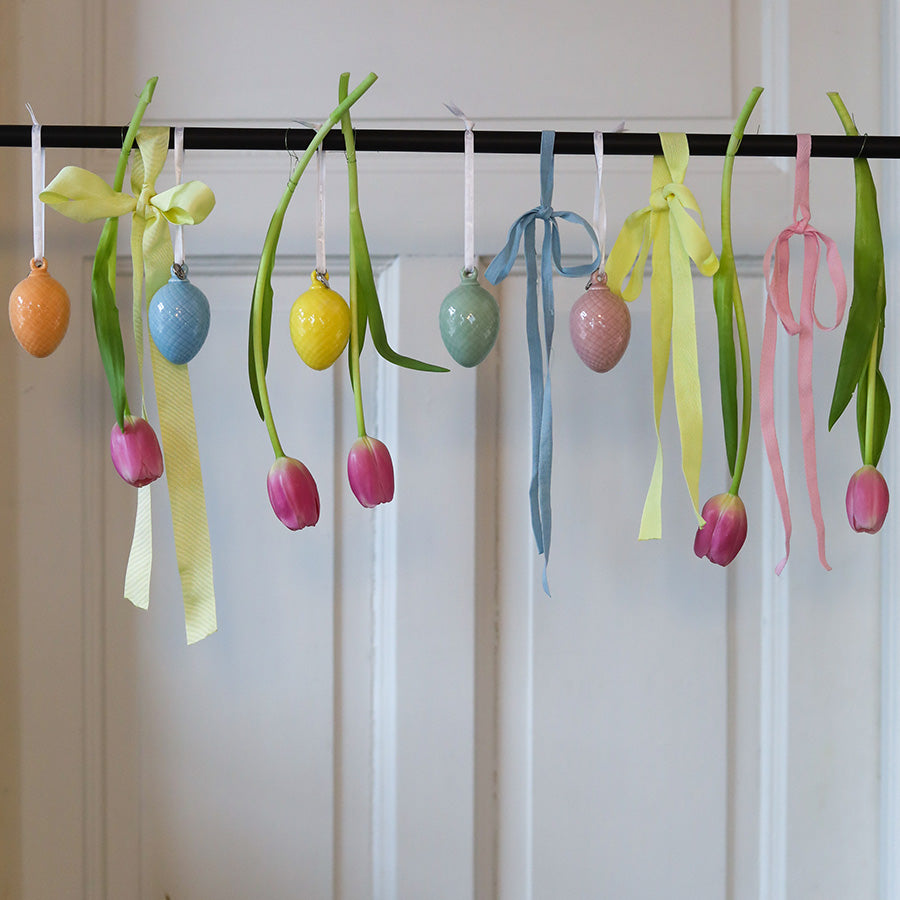 Vakkert dekorert med porselensegg hengende sammen med tulipaner og bånd i friske farger, ideelt for påskefeiring.