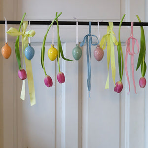 Vakkert dekorert med porselensegg hengende sammen med tulipaner og bånd i friske farger, ideelt for påskefeiring.