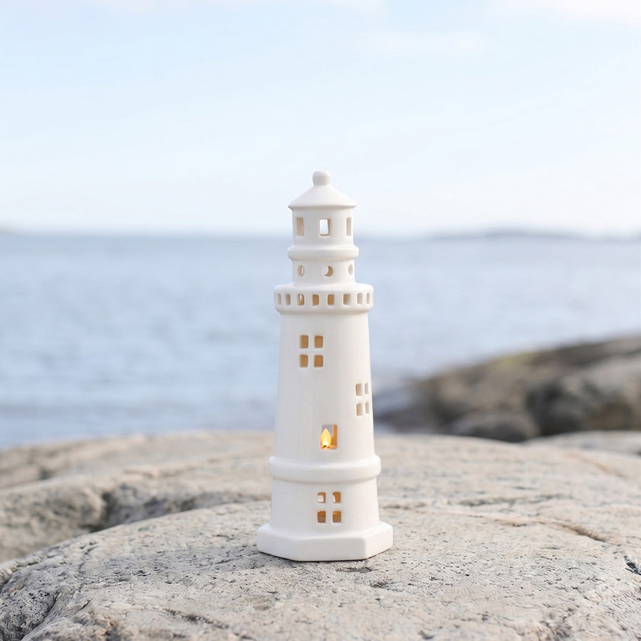 Dekorativt hvitt fyrtårn med LED-belysning plassert på en stein ved kysten, som skaper en stemningsfull atmosfære.