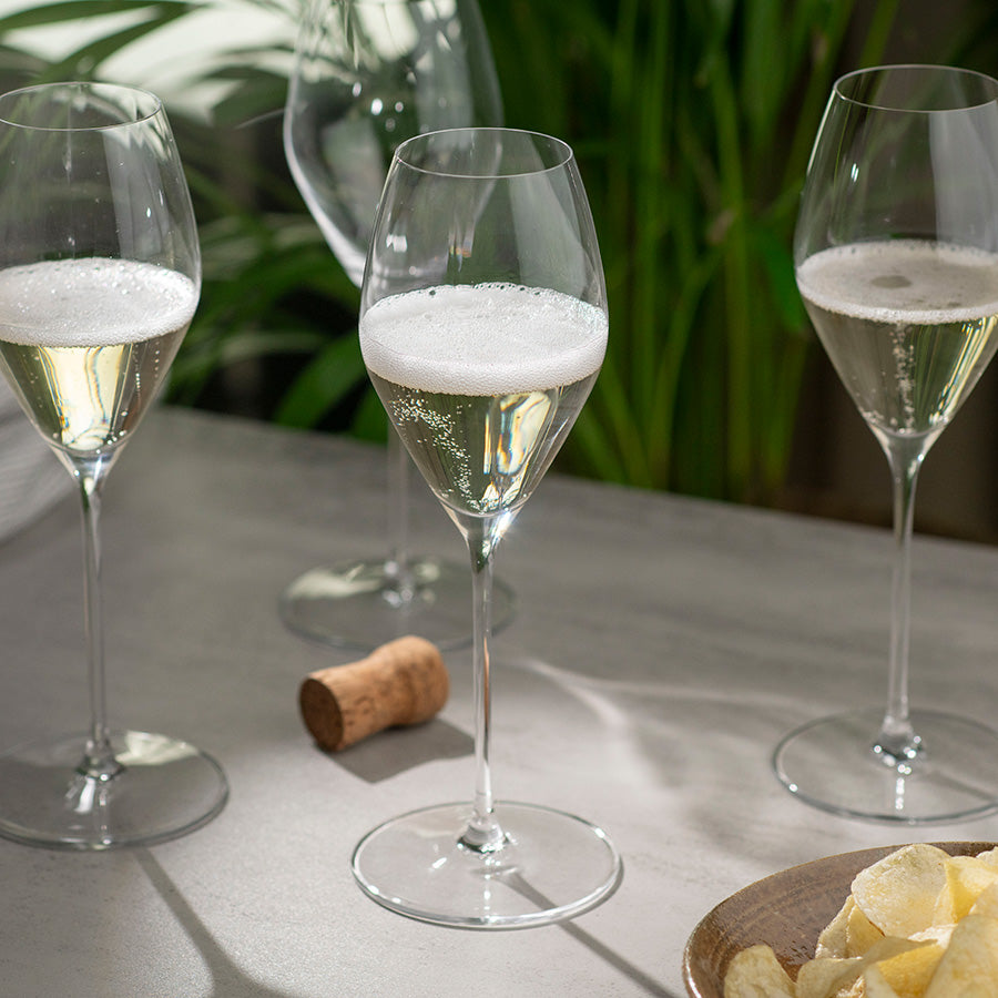 Riedel Performance champagneglass i bruk med bobler, omkranset av grønn flora, åpenbart ideelt for servering av champagne og musserende viner.