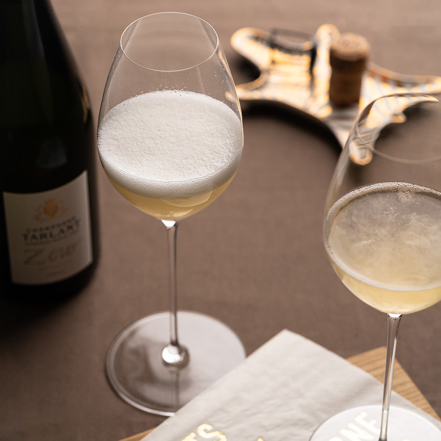 Riedel Superleggero champagneglass fylt med bobler, servert på bord med champagneflaske i bakgrunnen, ideelt for festlige anledninger.