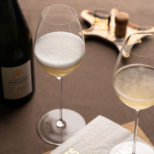 Riedel Superleggero champagneglass fylt med bobler, servert på bord med champagneflaske i bakgrunnen, ideelt for festlige anledninger.