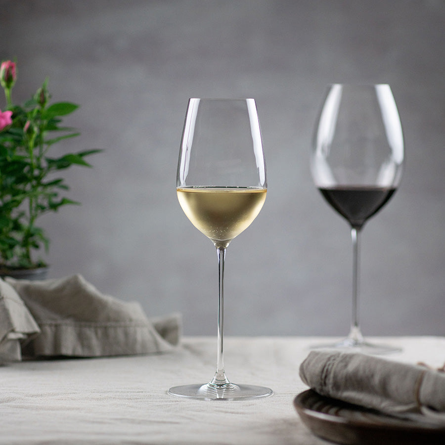 Riedel Superleggero allroundglass med hvitvin og et annet glass med rødvin i bakgrunnen, ideelt for vinelskere som setter pris på kvalitet.