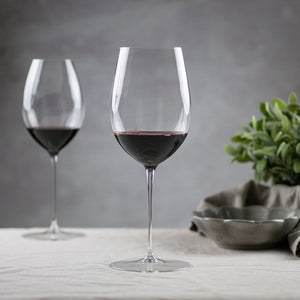 To Riedel Superleggero rødvinsglass med fyldig rødvin, plassert på en bordoverflate, fremhevende elegant design og høykvalitets krystall.