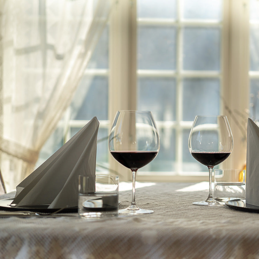 To Riedel rødvinsglass på et lyst bord, perfekt for å nyte Pinot Noir i hyggelige omgivelser.