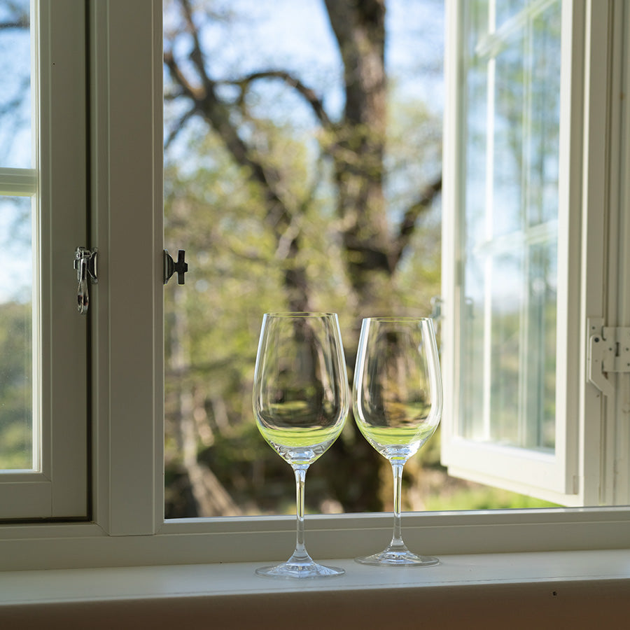 To tomme vinglass plassert på vinduskarmen, med utsikt mot et grønt trelandskap, ideelt for å nyte fine viner.