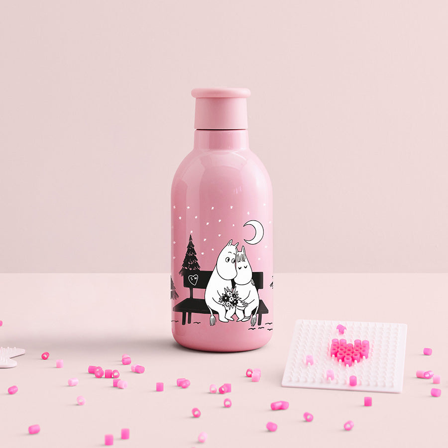Stelton Drink-IT Mummi termoflaske 0,5L i rosa på et rosa bord, med små perler og en hjerteformet figur ved siden av.