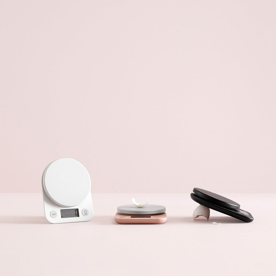 Tre kjøkkenvekter i forskjellige farger, inkludert svart, hvit, og rosa, illustrerer variasjonen i RigTig kjøkkenvekter.