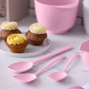 Rosa gryteskjeer og slikkepotter ved siden av muffins og bakeutstyr