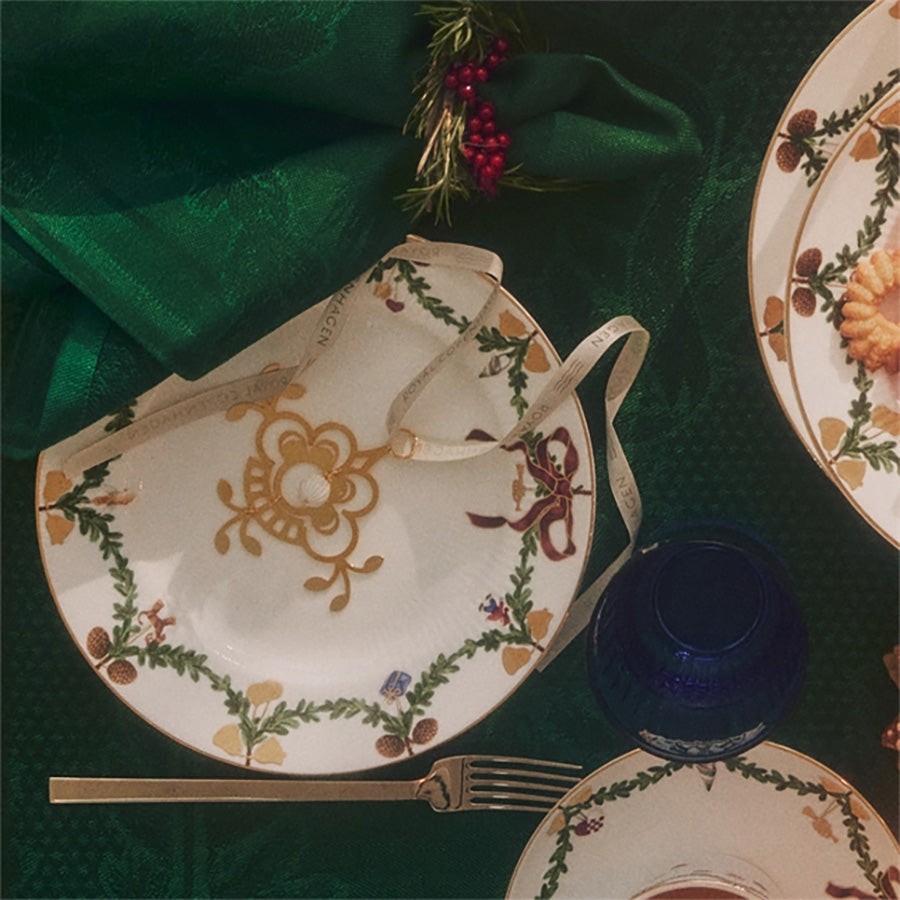 Stilig julepynt som ligger på en juledekket tallerken sammen med annen dekorasjon, som illustrerer den festlige atmosfæren.