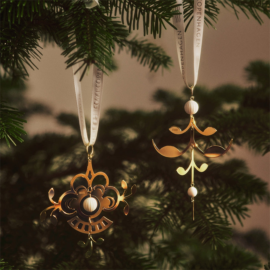 To vakre julepynt fra Royal Copenhagen henger på en juletregren, i en koselig og festlig setting.