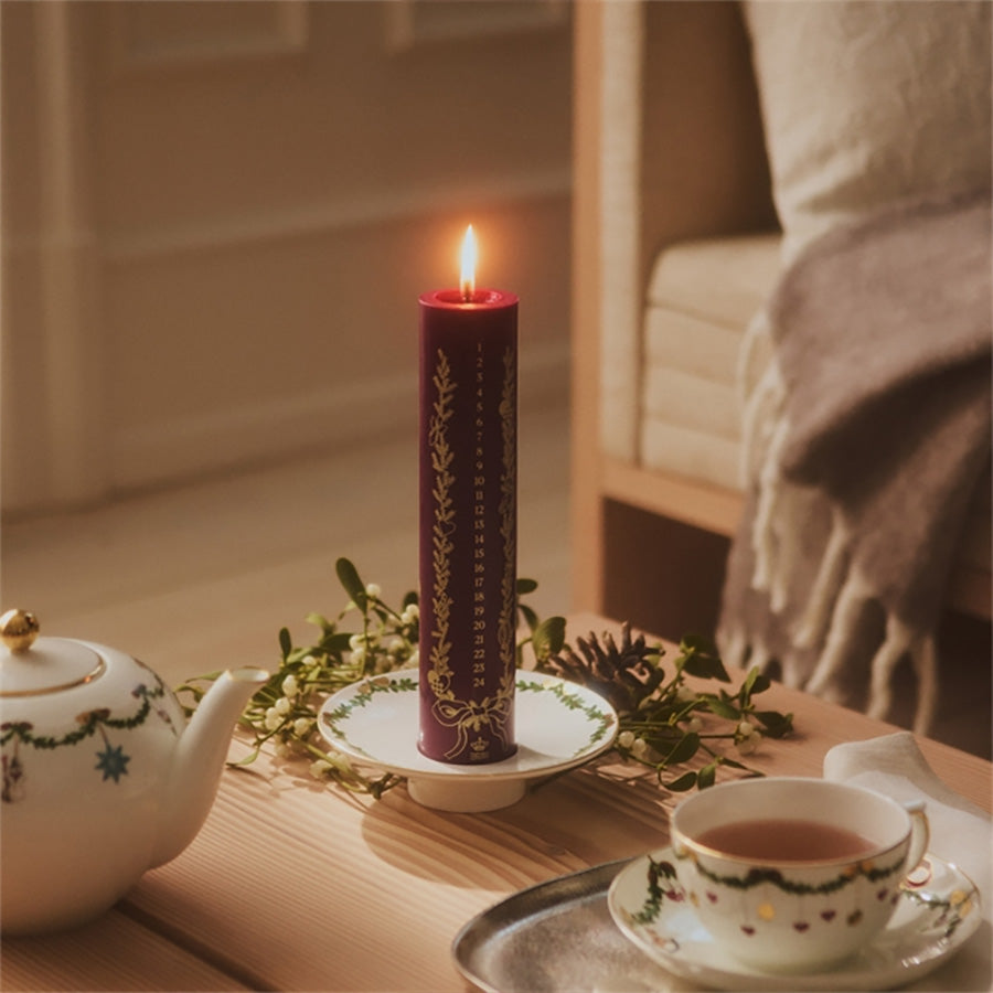 Stemningsfullt bilde av Royal Copenhagen kalenderlys tent på et bord med te, dekorative elementer og julestemning.