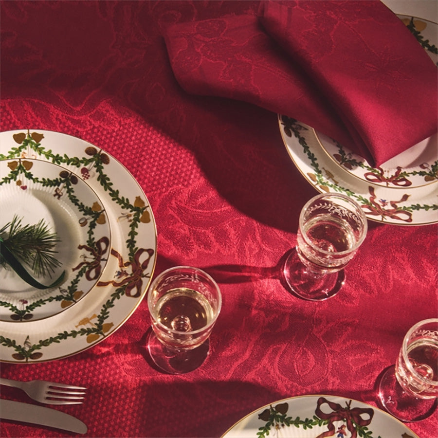 Elegant borddekk med røde stoffservietter fra Royal Copenhagen, kombinert med porselen og juledekorasjoner, perfekt for julemiddager.
