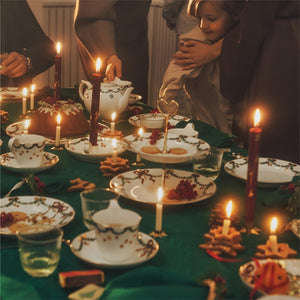 Familie som samles rundt et bord med stearinlys og festlig juledekorasjoner, som skaper en varm og innbydende atmosfære.