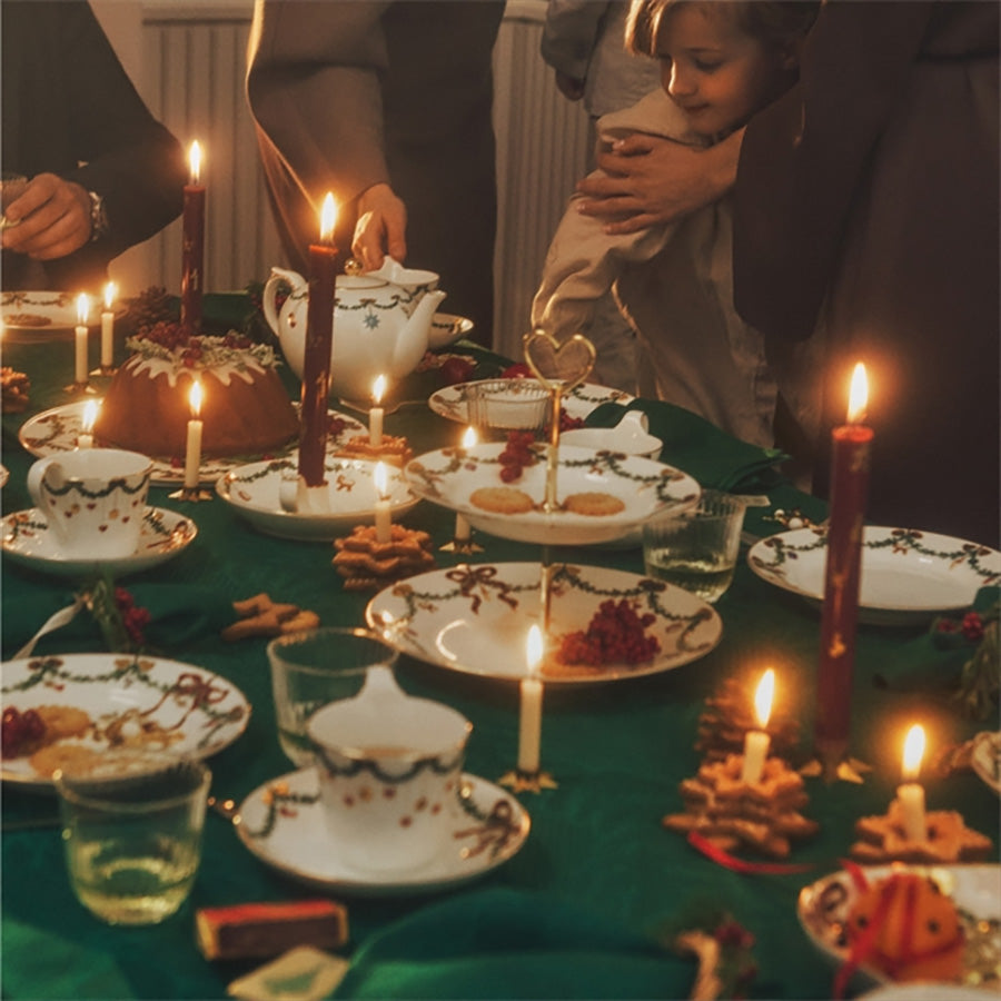 Familie som samles rundt et bord med stearinlys og festlig juledekorasjoner, som skaper en varm og innbydende atmosfære.