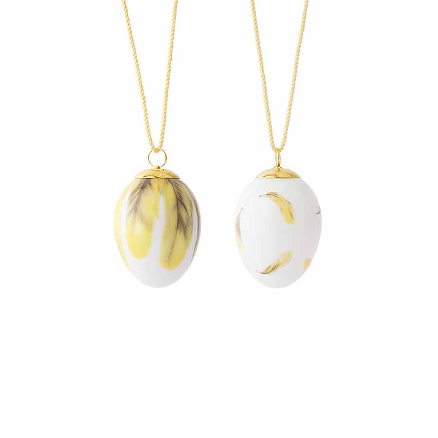 Royal Copenhagen eksklusivt sett med to dekorative egg designet med pirolfjær. Det ene egget har gule fjær mot en hvit bakgrunn, mens det andre egget er hvitt med delikate motiver av fjær. Ideell som vår- og påskepynt.