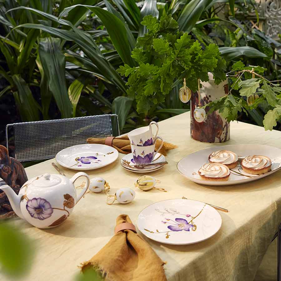Royal Copenhagen borddekorasjon med Vårkolleksjon 2025 egg, blomsterkopper, tallerkener og kaker på et bord dekket med grønt miljø.