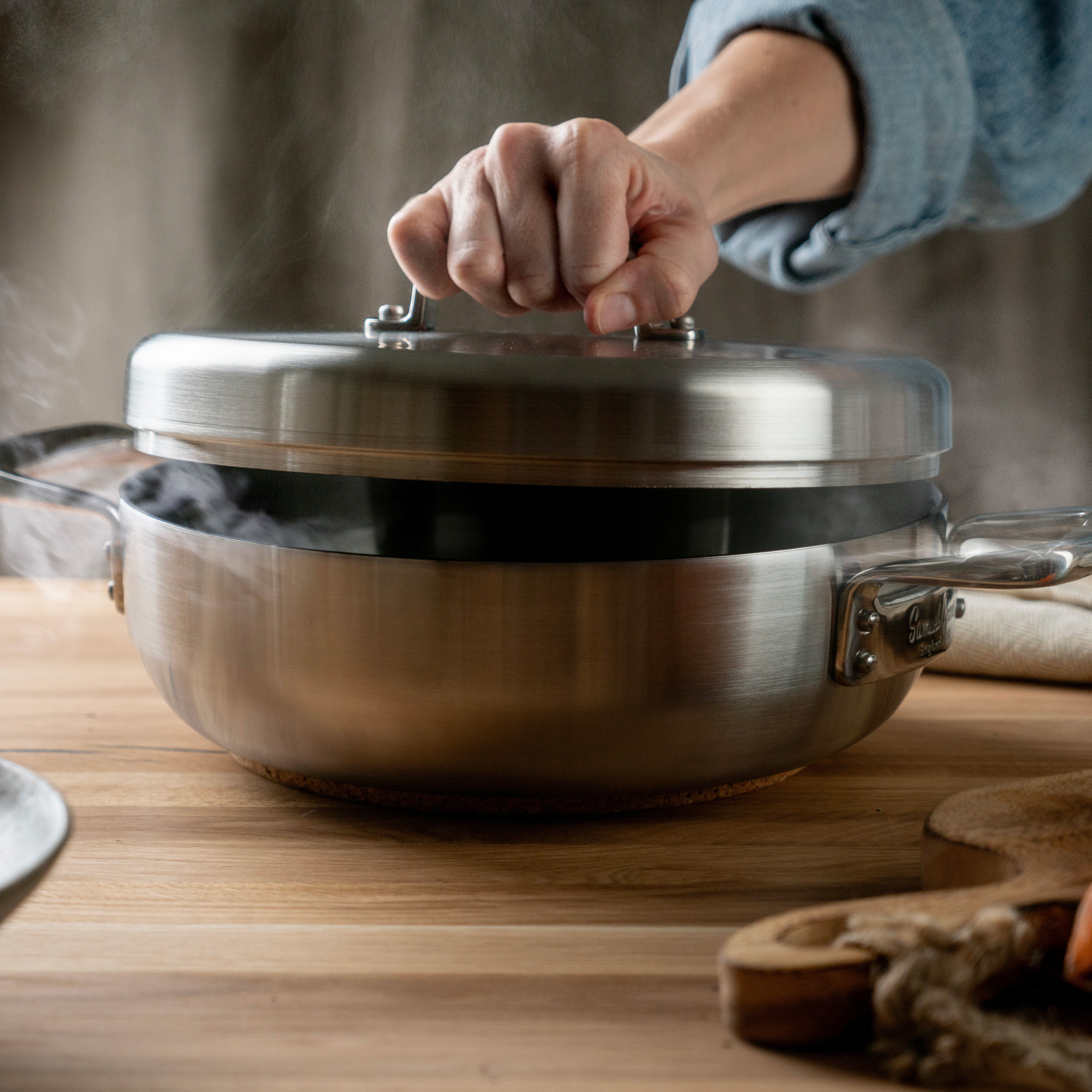 Hånd som løfter lokket på Samuel Groves sautépanne, som frigir damp og aroma under matlaging.