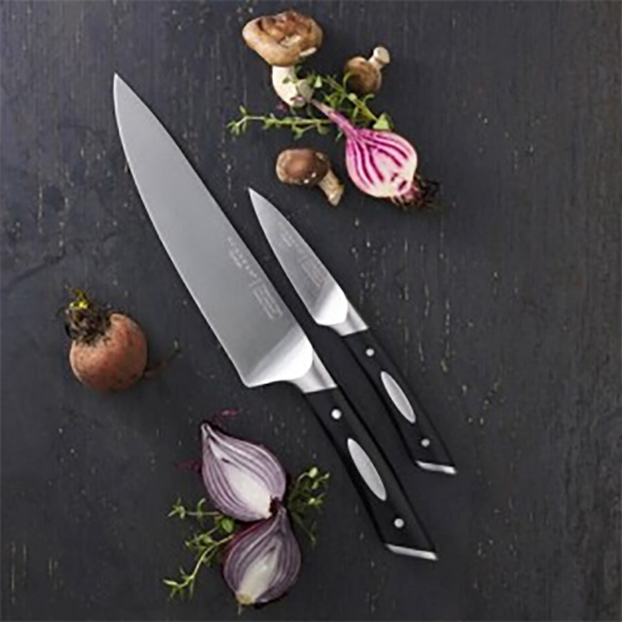 Scanpan Classic knivsett presentert med 20 cm kokkekniv og 9 cm grønnsakskniv, omringet av matvarer som sjampinjong og løk på en bordplate.