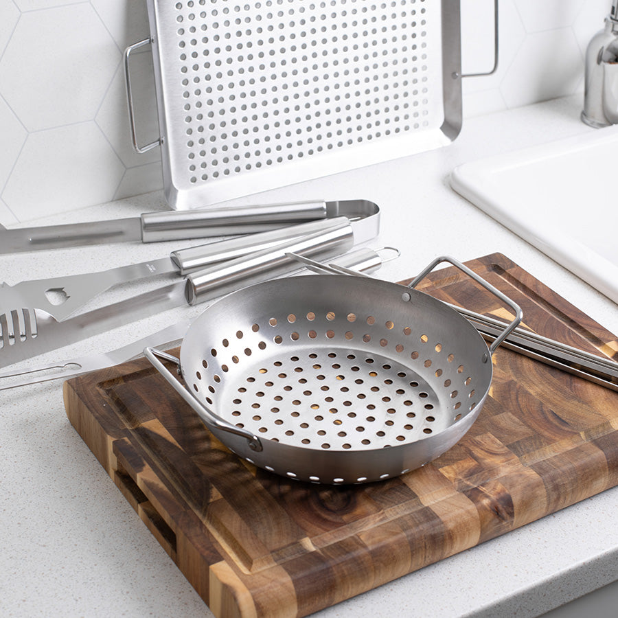 Rund grillform i rustfritt stål med perforerte hull, ideell for trygg grilling av sjømat og grønnsaker, plassert på et skjærebrett.