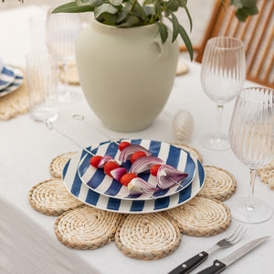 Festlig dekket bord med Seasons grillspyd som inneholder tomater og grønnsaker på en stripete tallerken, omgitt av elegante glass og en vase med planter.