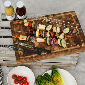 Seasons grillspyd med grilla grønnsaker og kjøtt på et skjærebrett, perfekt for grilling og servering. Nyttige tilbehør som BBQ-saus og dressing er synlige i bakgrunnen.
