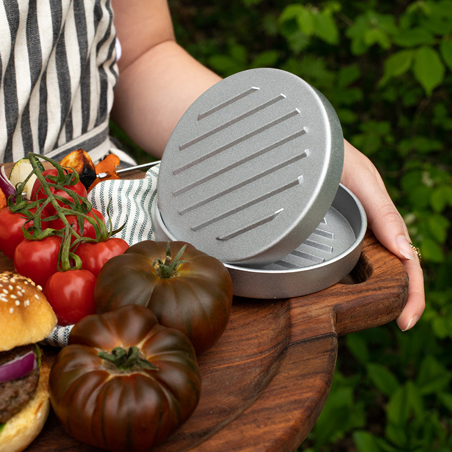 Seasons hamburgerpresse klar til bruk, omgitt av friske tomater og grønnsaker, ideelt til grilling.