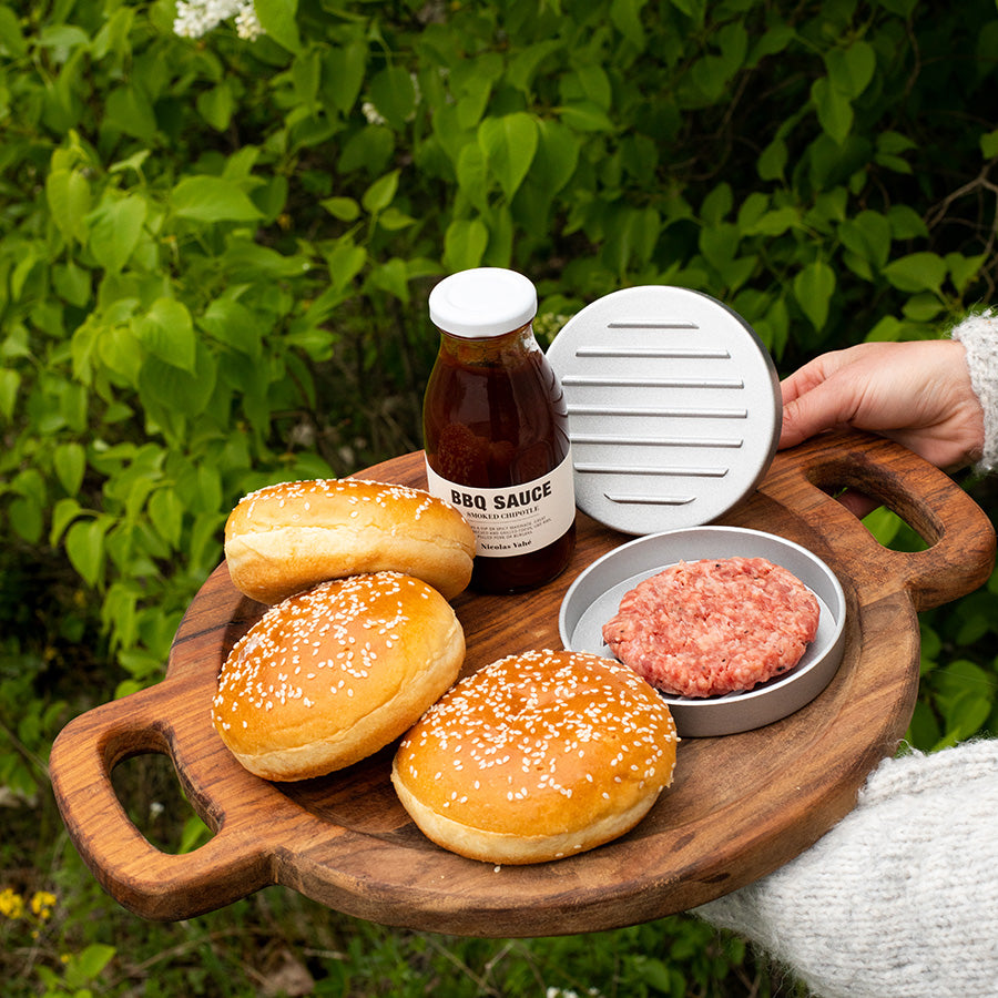 Tallerken med hamburgerbrød, BBQ-saus og hamburgerpresse, klart til grilling for en sommerfest.